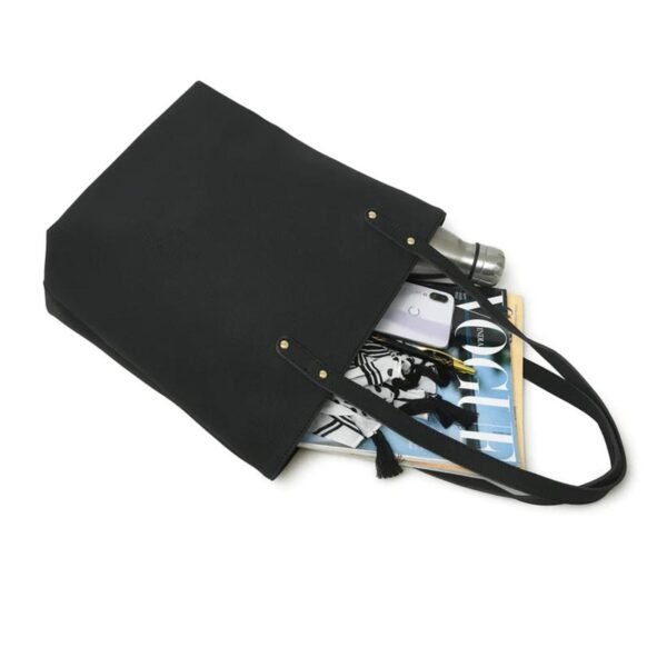 Black leather tote bag with long handles, partially open to reveal contents including a magazine, smartphone, and stainless steel water bottle, against a white background