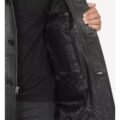 Close-up view of the interior of a black leather coat, highlighting the quilted lining and a large inner pocket, with a person holding the coat open to display the detailing