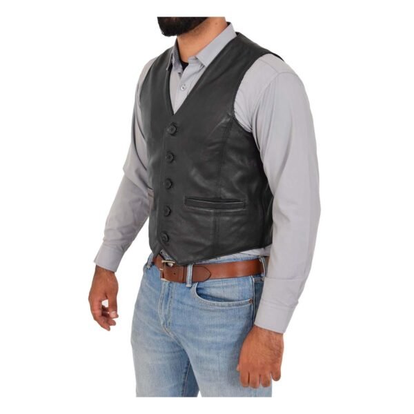 Side tilted view of a man wearing a black leather vest over a light gray button-up shirt, paired with blue jeans and a brown leather belt