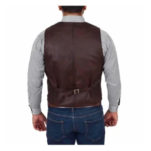 Back view of a man wearing a brown leather vest over a light gray button-up shirt, paired with blue jeans and a brown leather belt