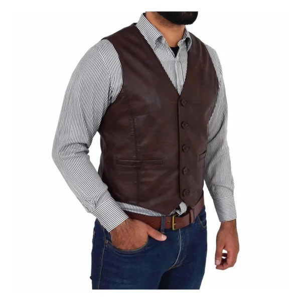 Side tilted view of a man wearing a brown leather vest over a light gray button-up shirt, paired with blue jeans and a brown leather belt