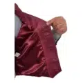 Close-up view of a hand holding open a burgundy leather vest, showcasing the smooth inner lining and buttonhole details