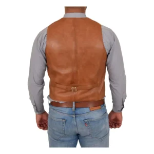 Back view of a man wearing a tan leather vest over a light gray button-up shirt, paired with blue jeans and a brown leather belt