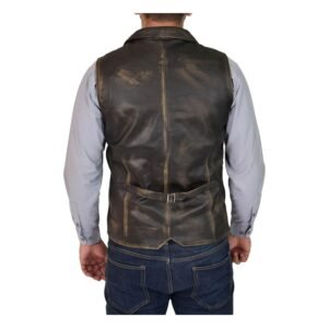 Back view of a man wearing a distressed black leather vest over a gray long-sleeve shirt, paired with dark blue jeans, highlighting the adjustable strap and rustic texture of the vest