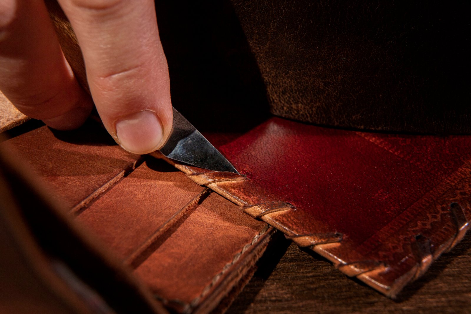 Close-up of a craftsman’s hand using a precision knife to cut and shape leather, showcasing the intricate details of leatherworking